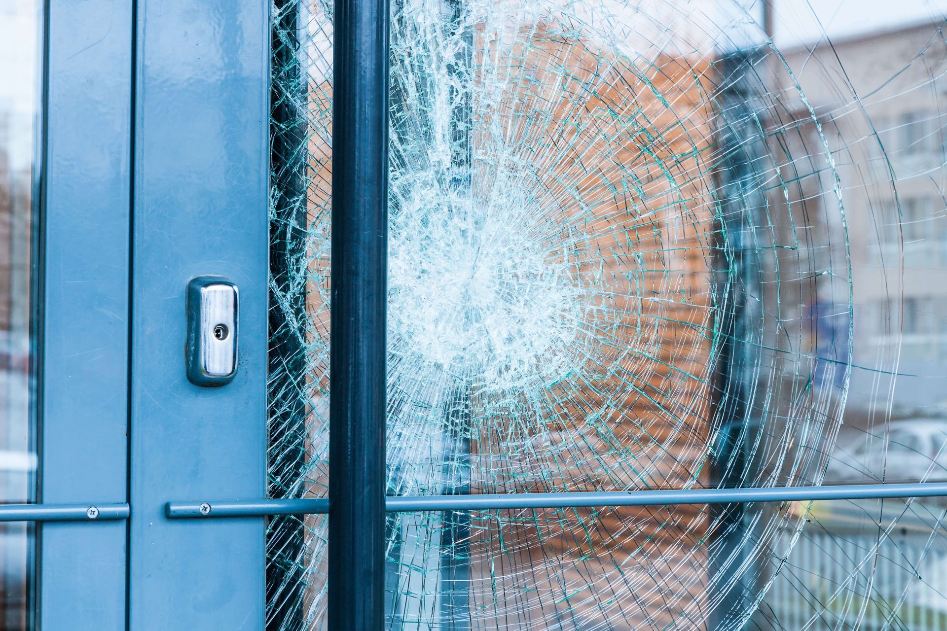 Shattered glass window in a blue metal door frame; a security button is visible.