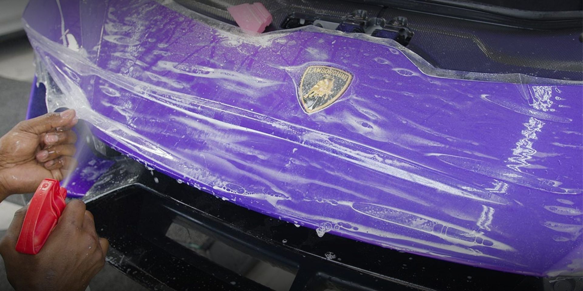 Applying a protective film to a purple Lamborghini bumper with a spray bottle.