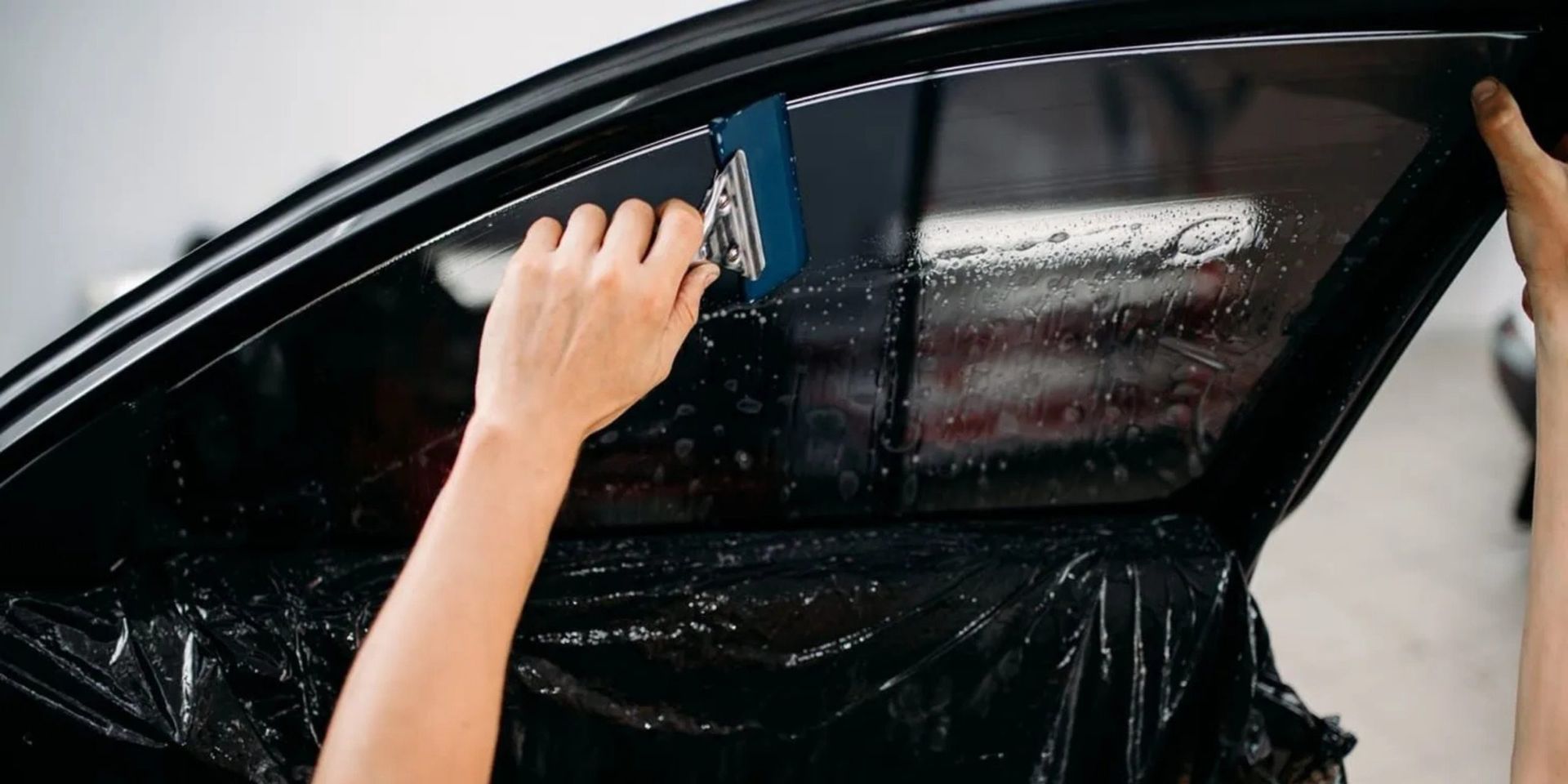Applying tinted film to a car window with a squeegee.