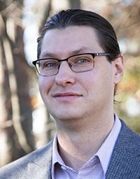 Man with glasses smiling, outdoors in a natural setting.