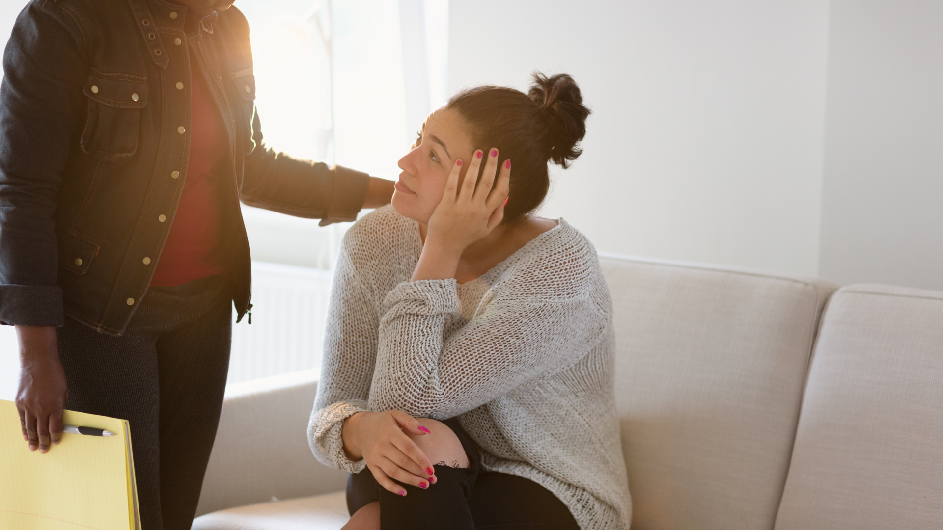 A man is comforting a woman who is sitting on a couch.