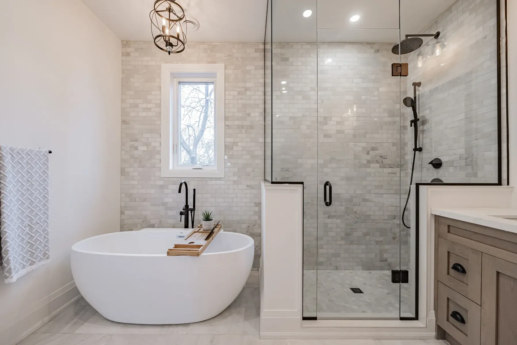 Elegant modern bathroom with a white soaking tub, glass shower, and gray tile walls.