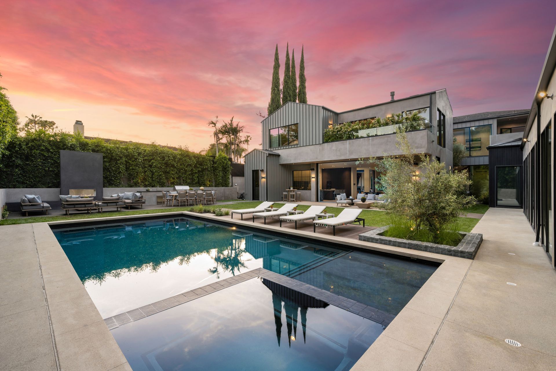 Luxury home with pool at dusk; orange and pink sunset, green lawn, modern architecture.