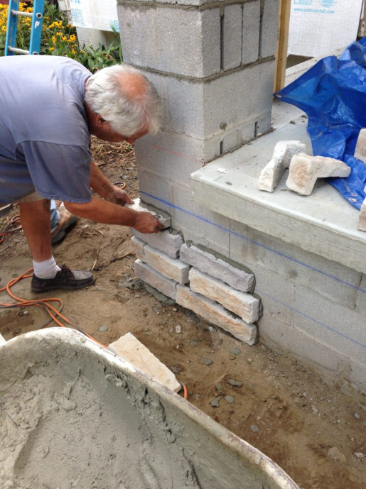 A man is laying bricks on a wall next to a blue tarp.