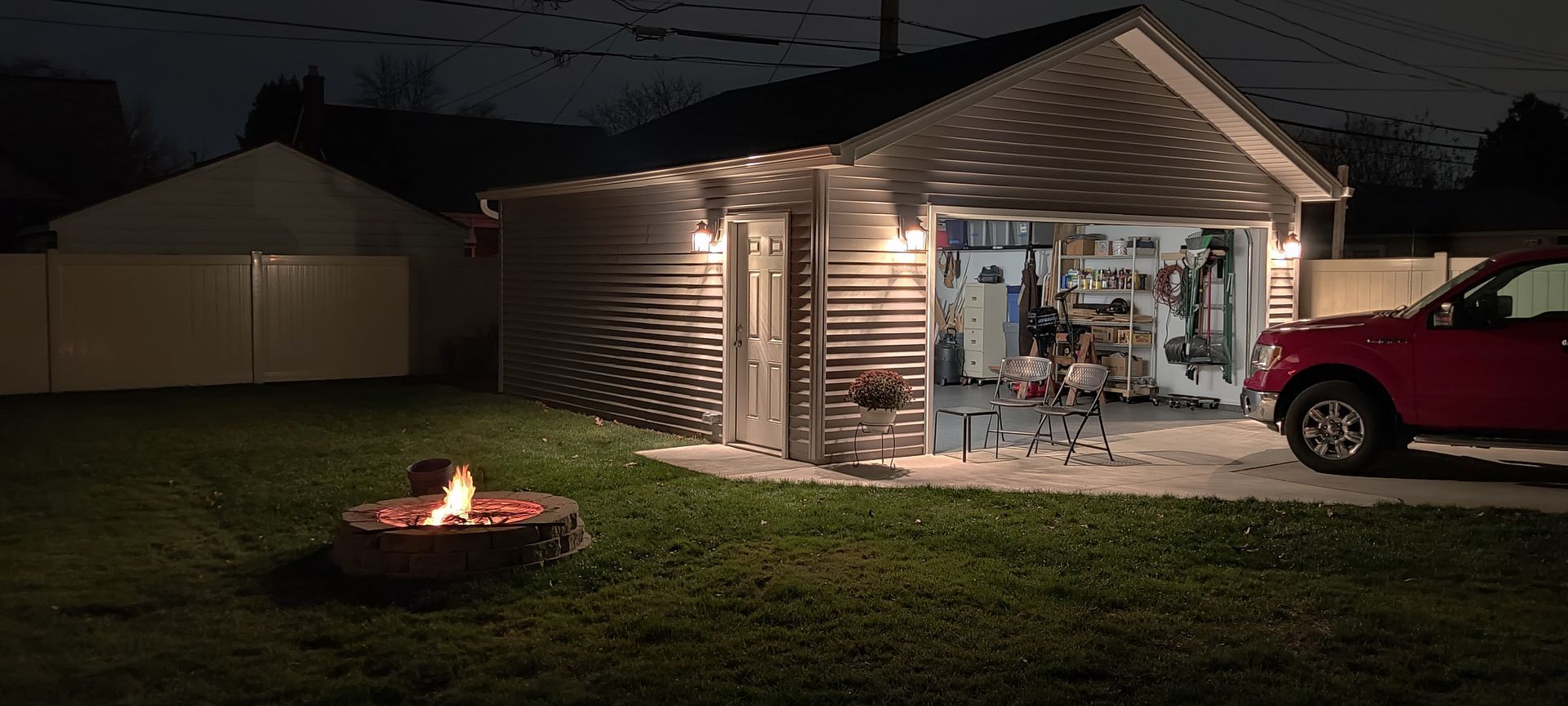 A red truck is parked in front of a house with a fire pit in front of it.
