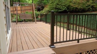 Wooden deck with brown railing, swing, and greenery in the background.