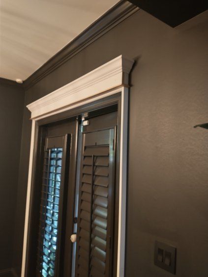 Dark door frame with white molding against a dark gray wall, featuring shutters.