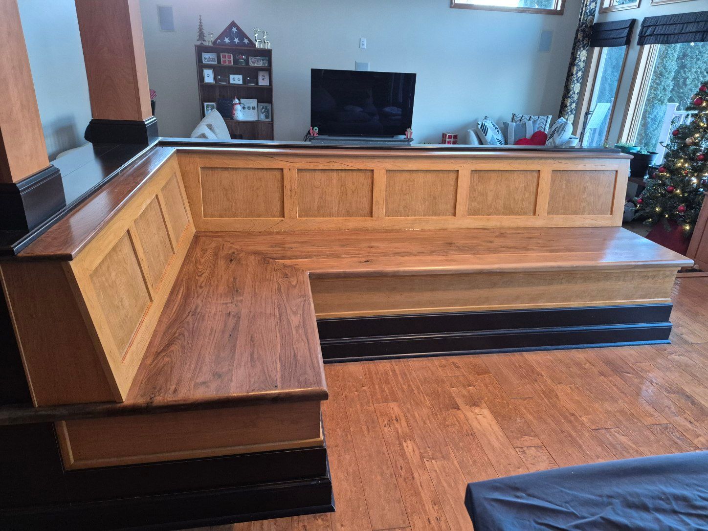 Wooden L-shaped built-in bench in a dining area. Features a dark stained base, light wood panels, and a dark tabletop.