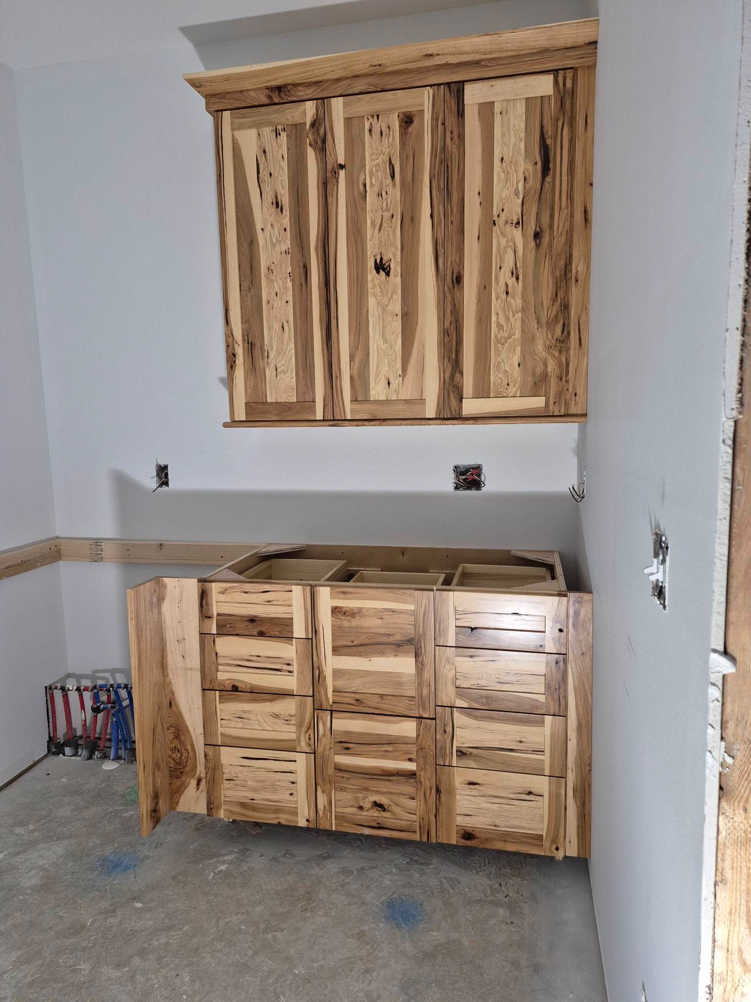 Light wood cabinets, installed on a gray wall. Upper cabinets above a lower cabinet set.