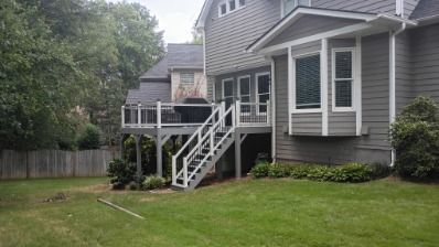 Gray house exterior with a deck, stairs, and a grassy backyard.