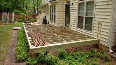 Wooden deck under construction next to a house with exposed framing and a green lawn.