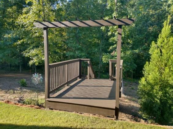 A brown wooden deck with a pergola in a grassy backyard.