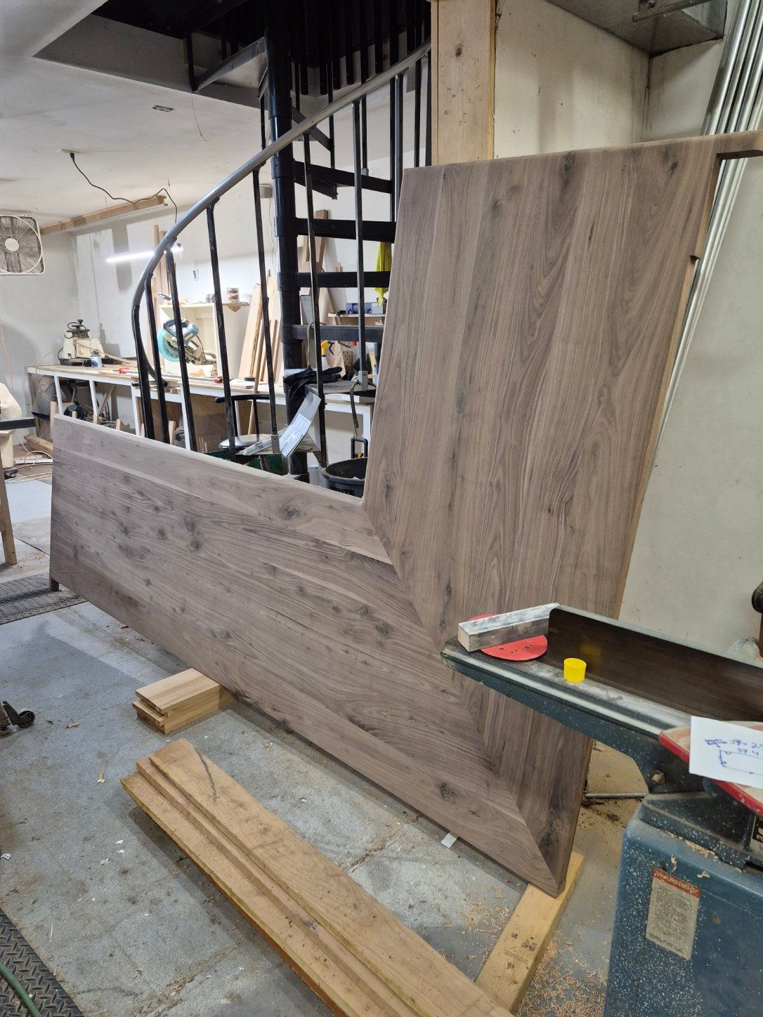 Large wooden panel leans against a workshop wall, spiral staircase in background.
