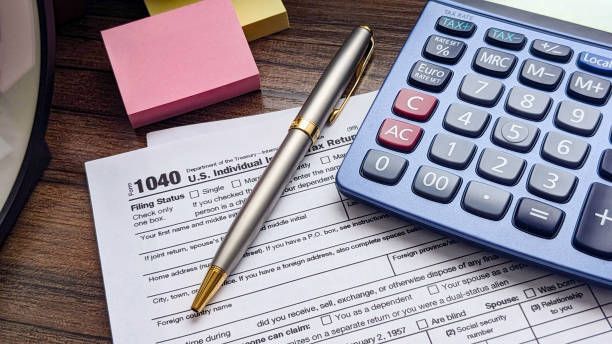 A pen is sitting on top of a tax form next to a calculator.