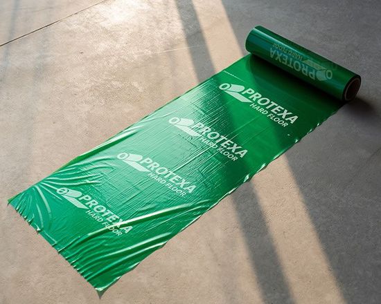 Groene rol Protexa vloerbeschermer die zich uitrolt op een betonnen ondergrond.