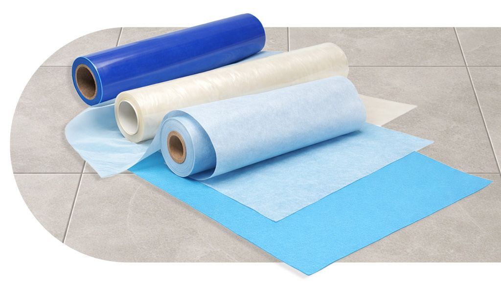 Vier rollen donkergrijs en goudkleurig bedrukt inpakpapier op een tegeloppervlak.