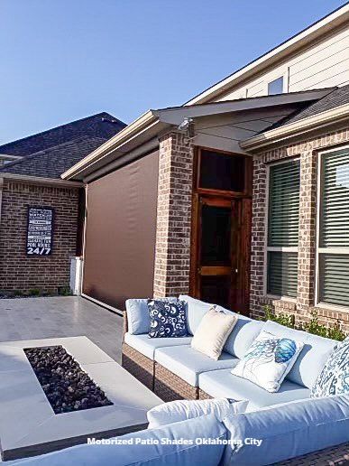 a patio with a couch and a fire pit in front of a brick house with mototirzed patio shades  Oklahoma City