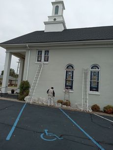 A man is painting the side of a building with a ladder.