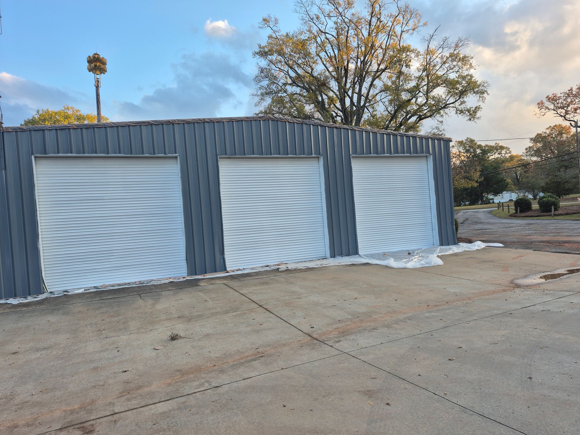 A garage with three white garage doors and a tree in the background.