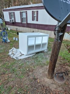 A white cabinet is sitting in the grass in front of a mobile home.