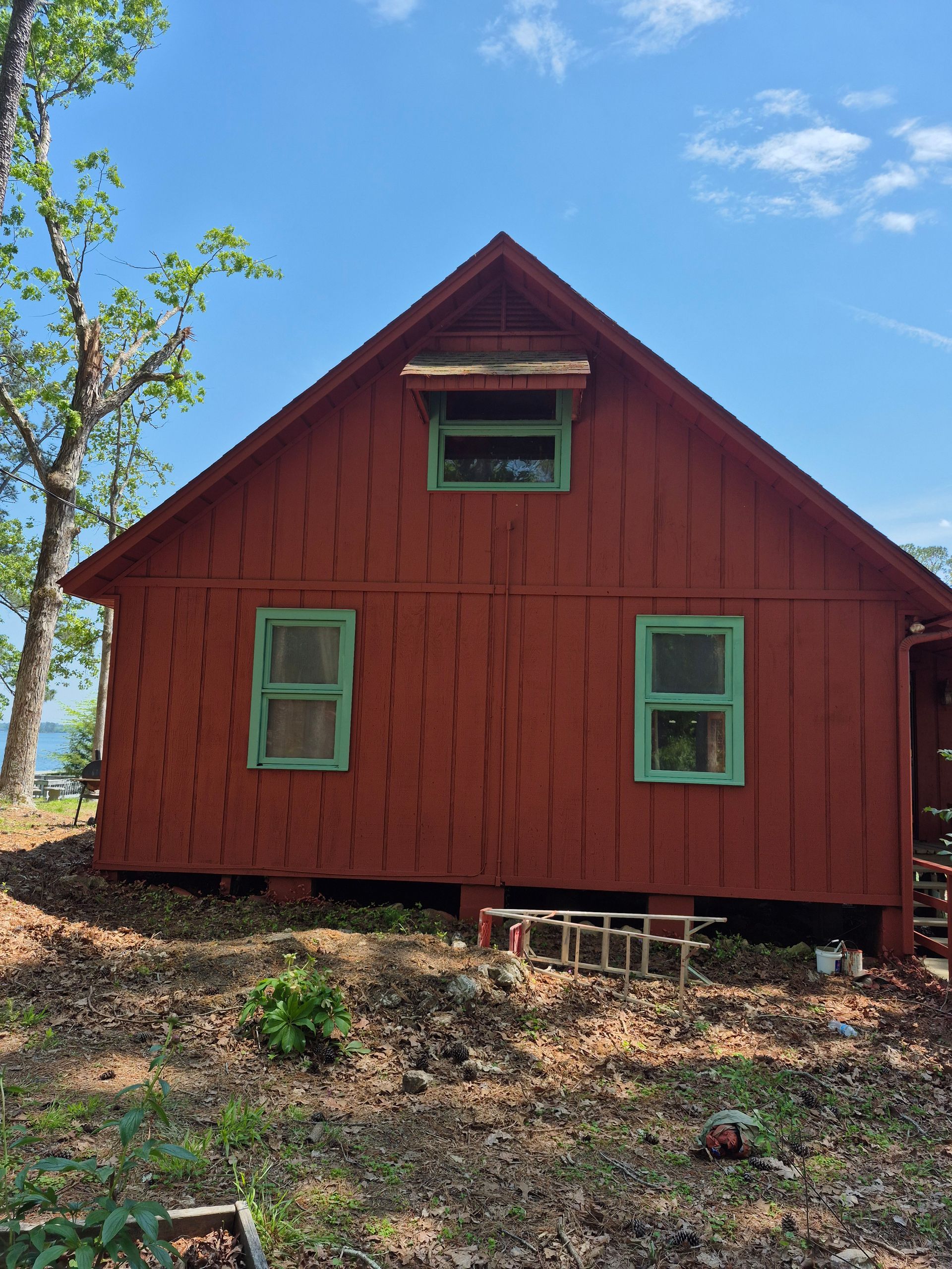 A red house with green windows is sitting on top of a dirt hill.