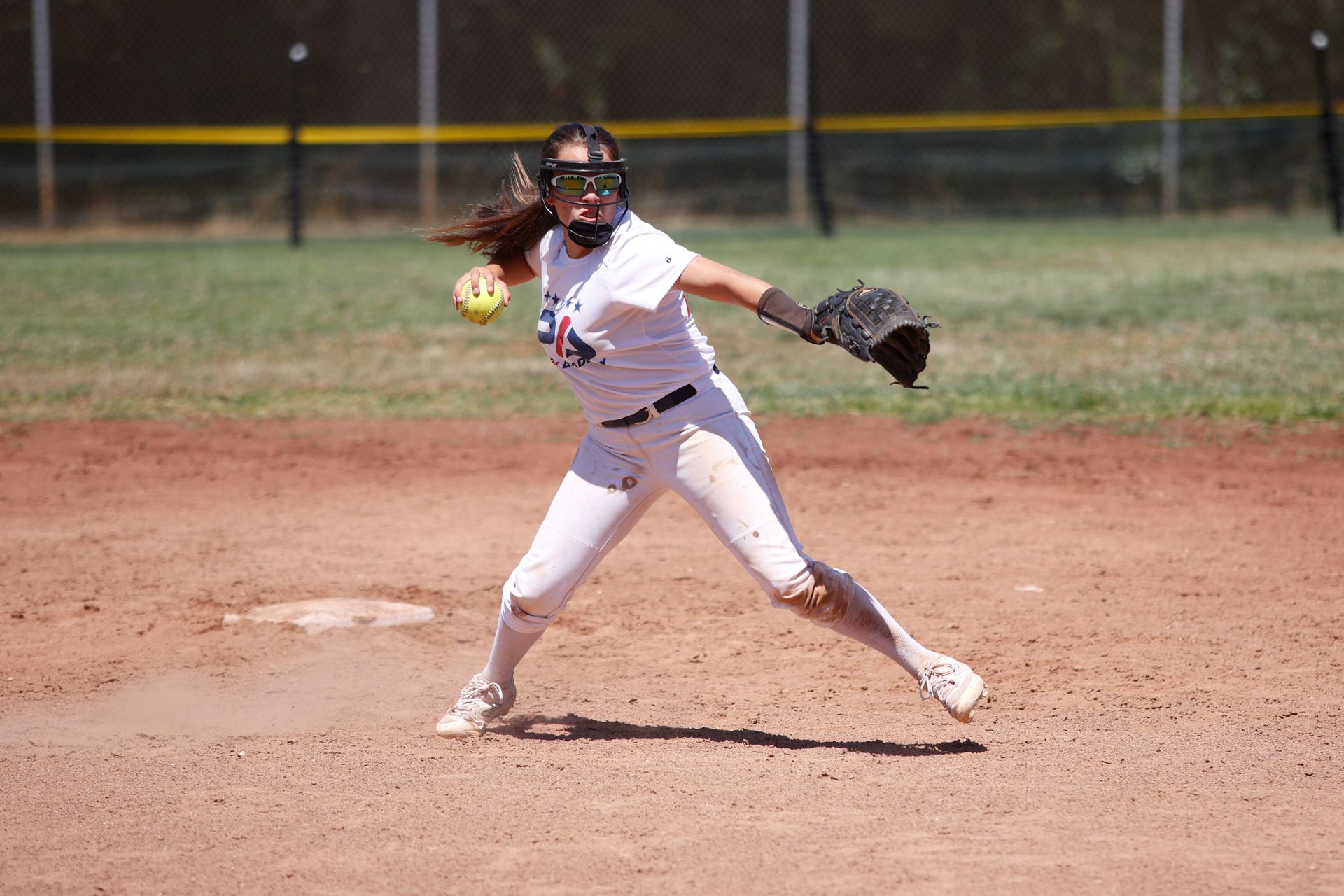 A woman is pitching a softball on a baseball field.