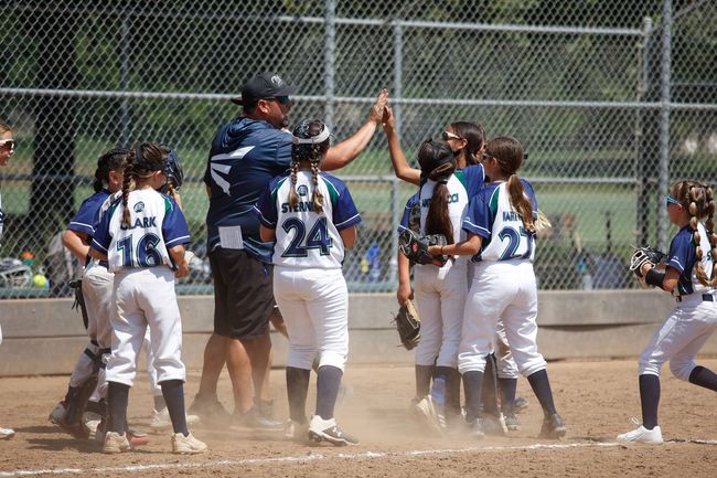 A group of young girls are giving each other a high five on a baseball field.