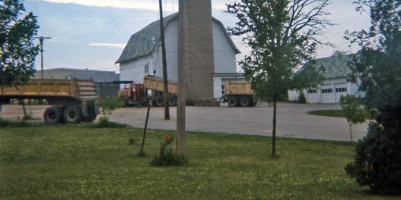 A dump truck is parked in front of a barn.