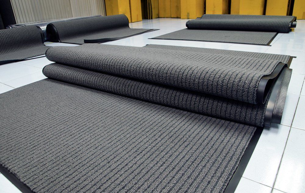 Rolled gray carpet samples displayed on a tiled floor in a showroom