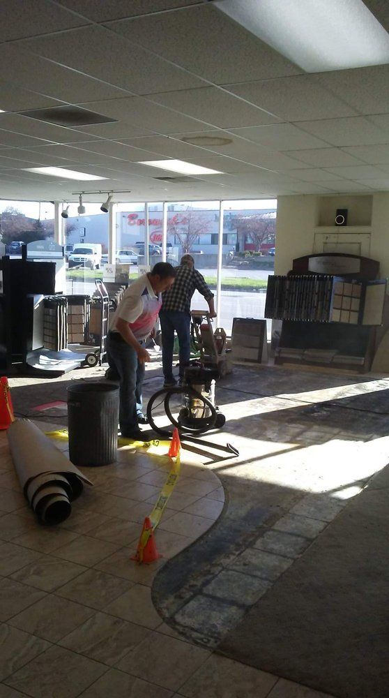 Two people in a gym entrance using a stationary bike near cones and sunlight from the windows.