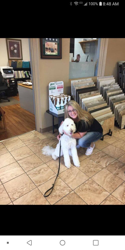 Woman kneeling and smiling beside a white dog in a lobby with record bins and tiled floor
