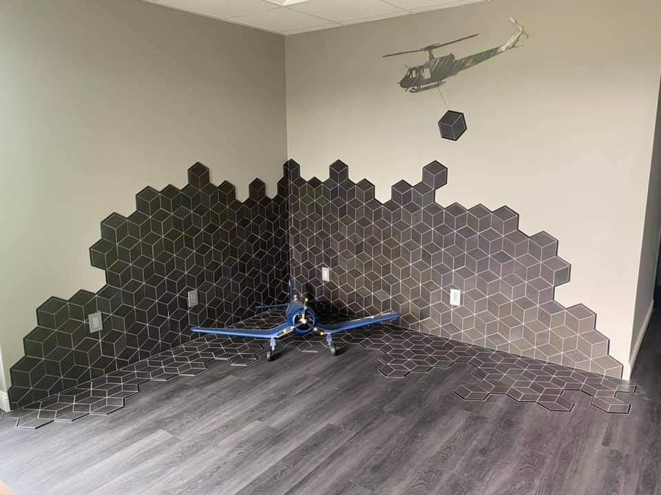 Small blue model helicopter in a corner with dark hexagon tile wall art and gray wood flooring