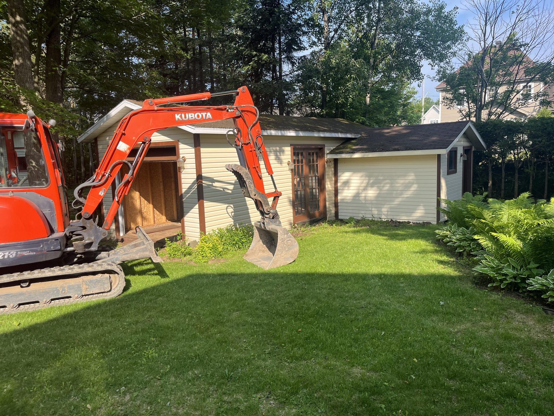 Une excavatrice rouge est garée dans l'herbe devant une maison.