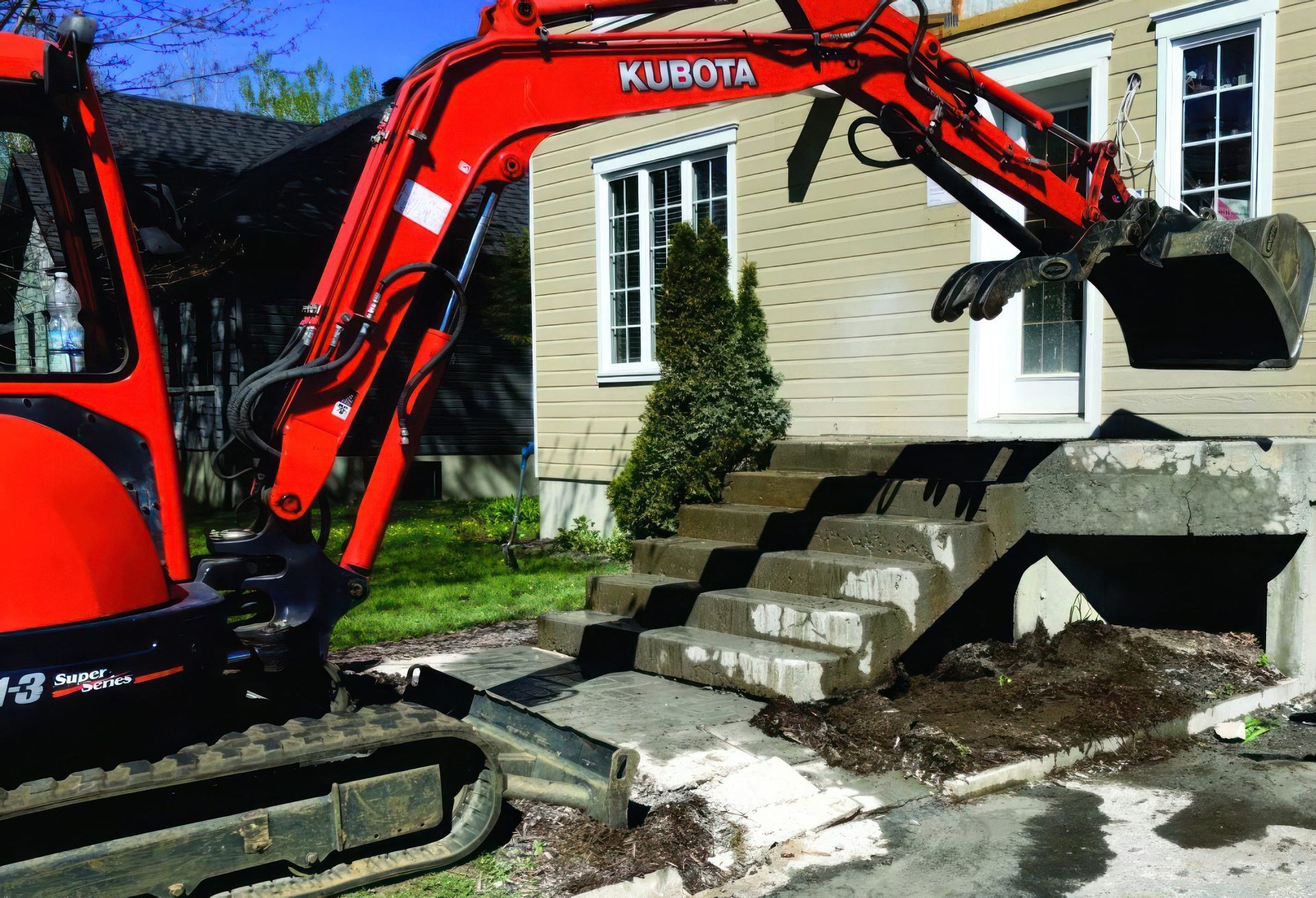 Une excavatrice Kubota rouge est garée devant une maison.