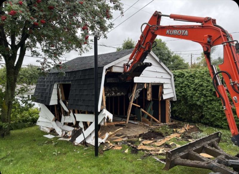 Une excavatrice Kubota démolit un garage dans une cour arrière.