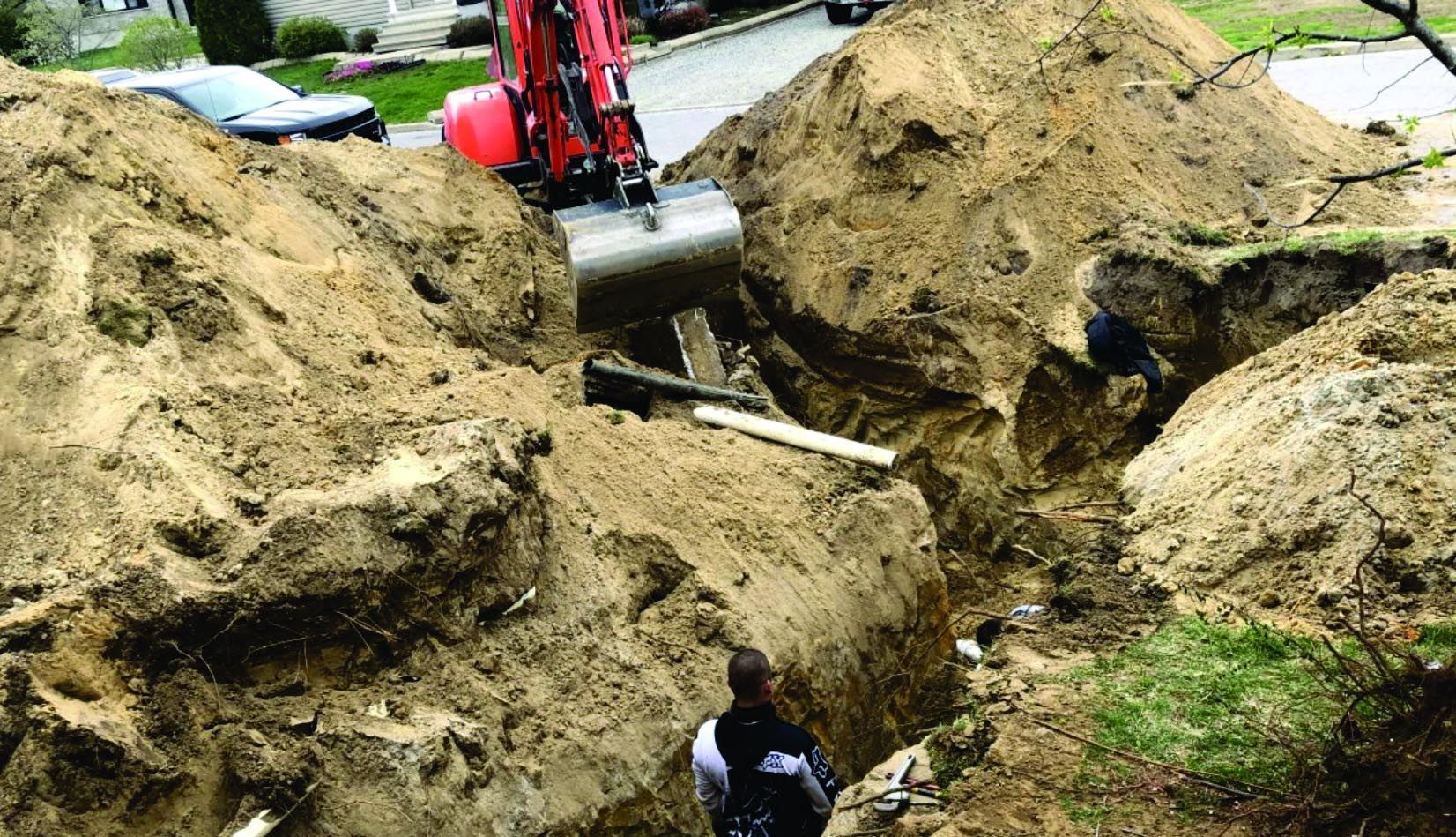 Un homme se tient debout dans une tranchée à côté d'un gros tas de terre.
