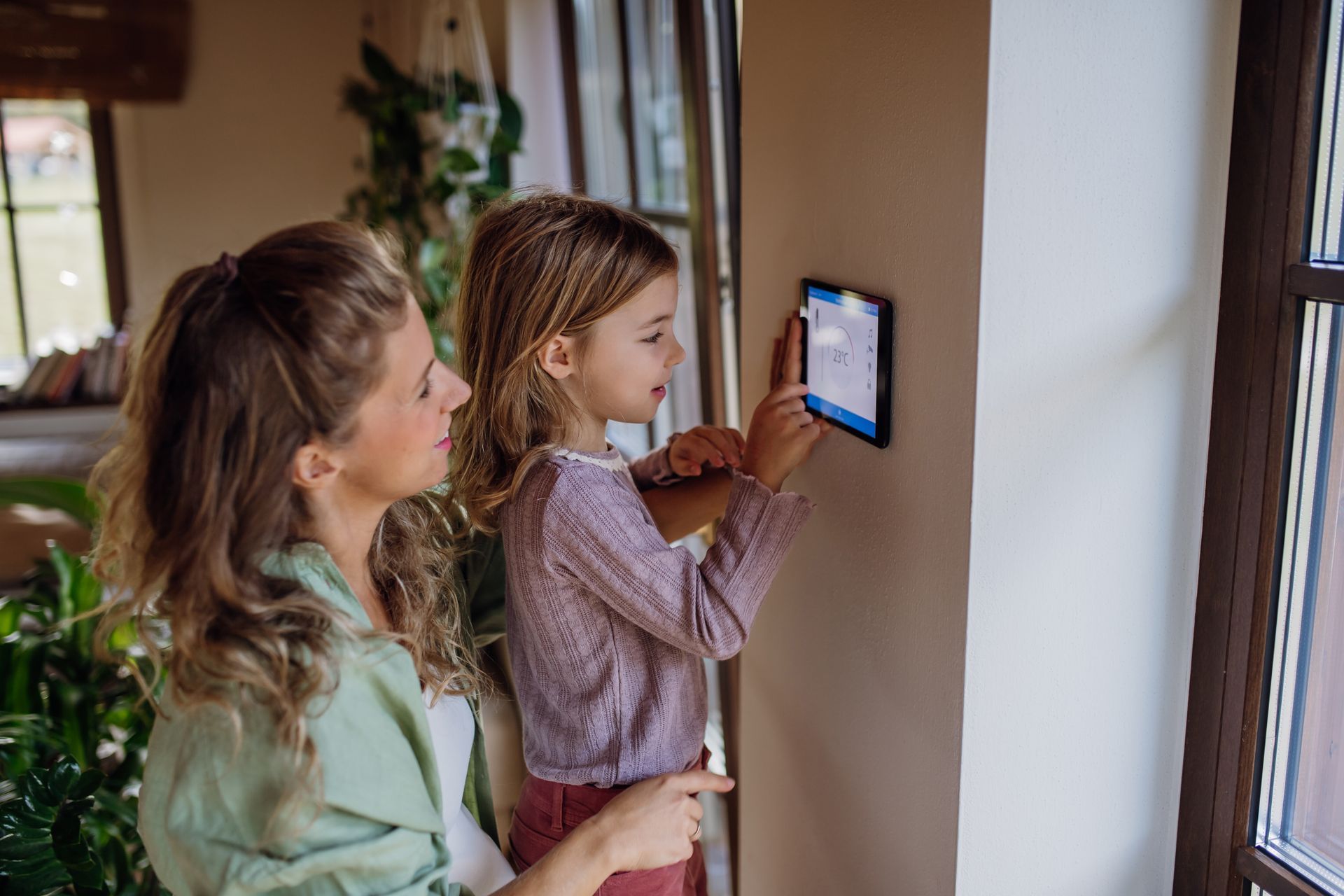 Woman and girl using a tablet mounted on a wall in a home, girl pointing at the screen.