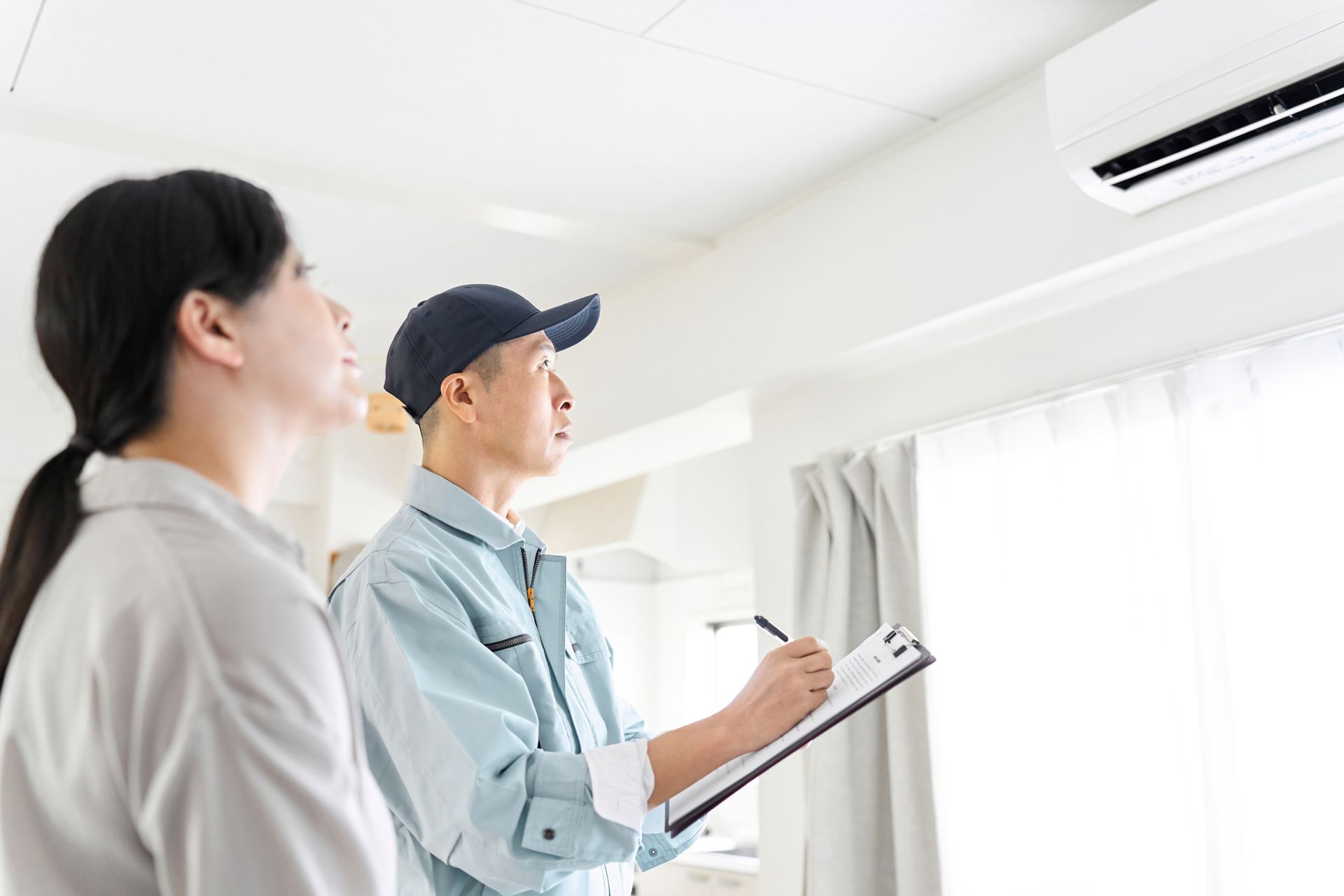 A man and a woman are looking at an air conditioner in a room.
