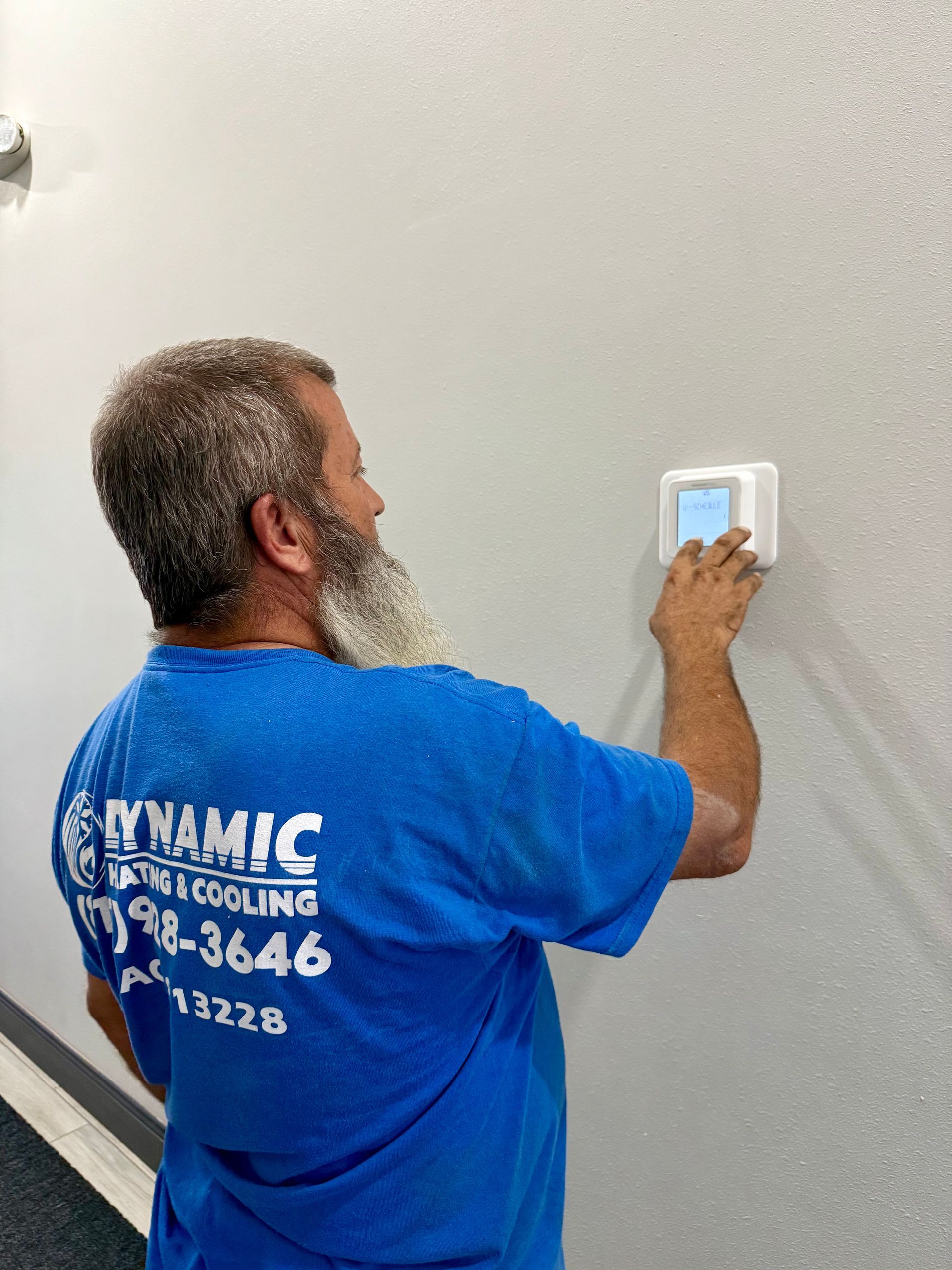 Man in blue shirt adjusting thermostat on a white wall.