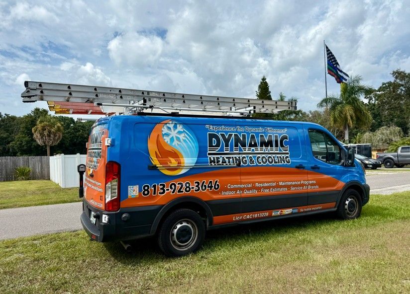 Dynamic Heating & Cooling van parked on grass, blue/orange logo, ladder on top, phone number visible.