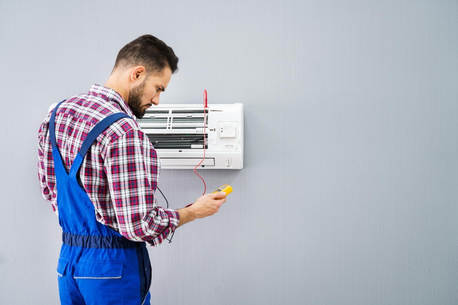 A man is fixing an air conditioner on a wall.