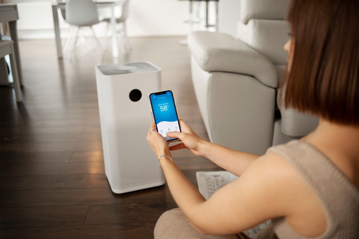 A woman is sitting on the floor using a smart phone to control an air purifier.