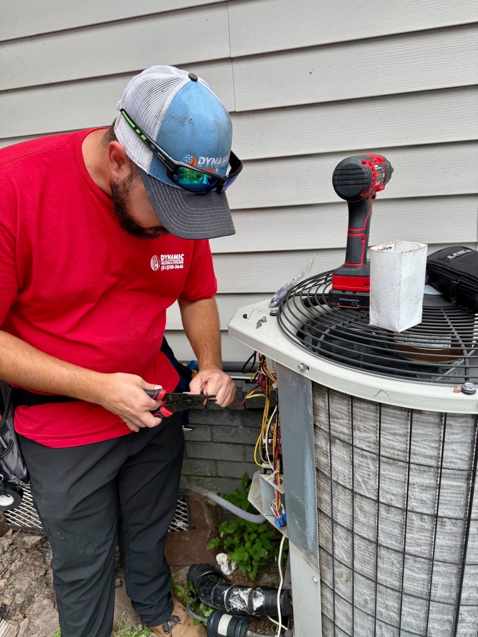 HVAC technician in red shirt and cap works on an air conditioning unit.