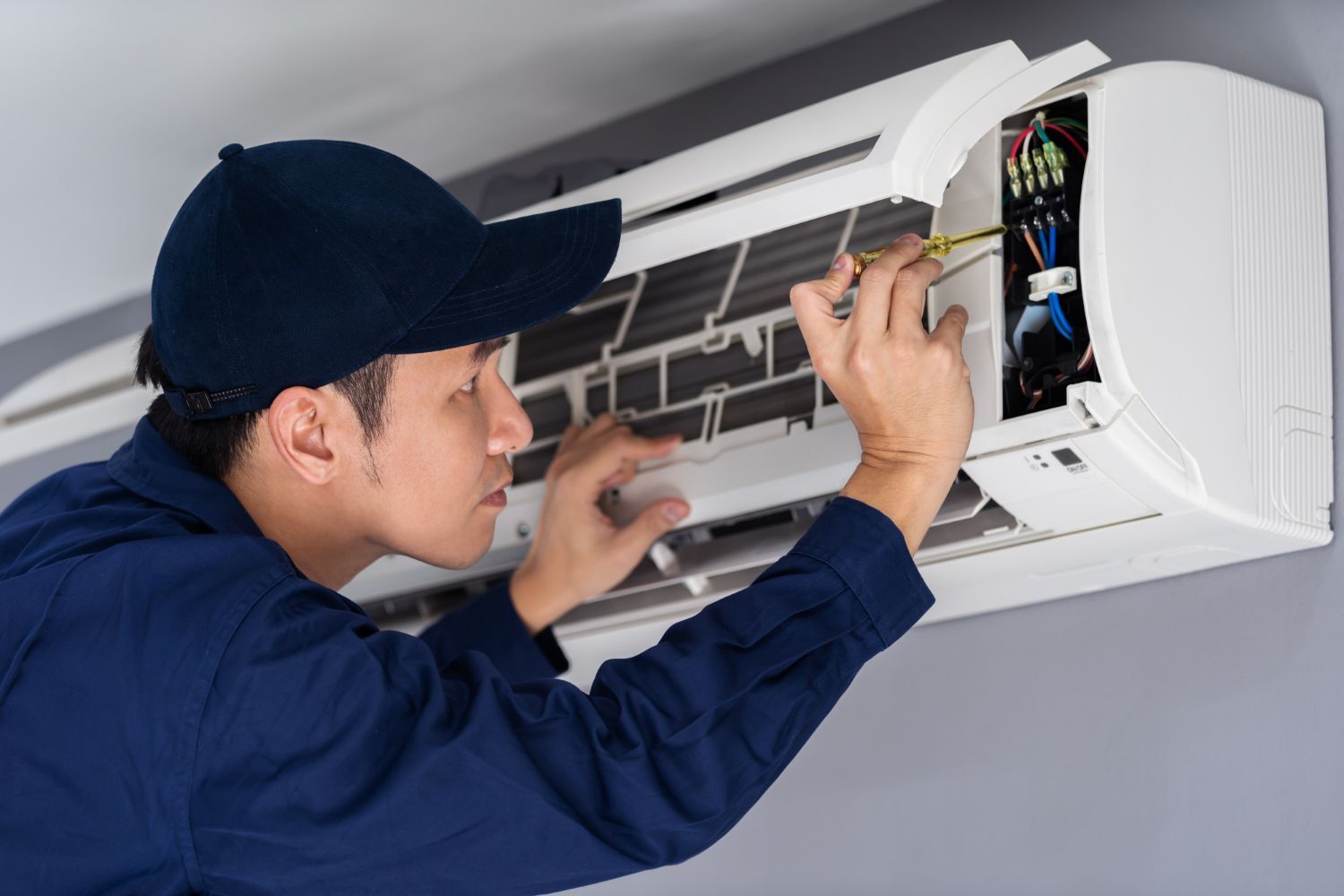 A man is fixing an air conditioner with a screwdriver.