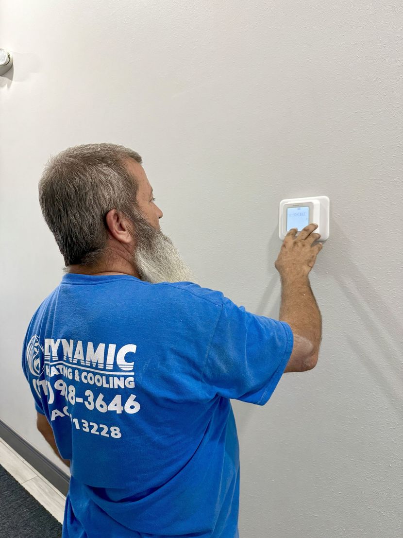 Man in blue shirt adjusting a thermostat on a white wall. The shirt reads 
