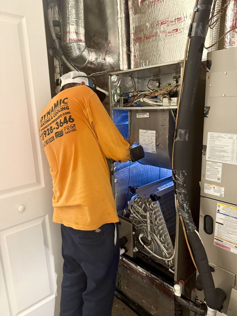 HVAC technician in orange shirt and hard hat repairs an air handler unit in a utility room.