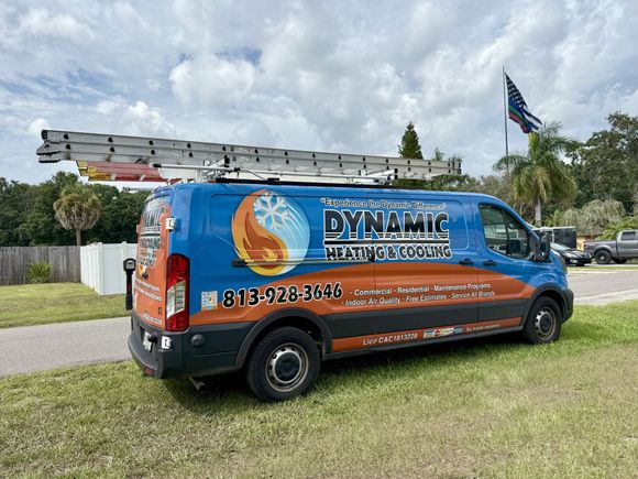 A blue and orange Dynamic Heating and Cooling service van parked on a lawn with a ladder on top.