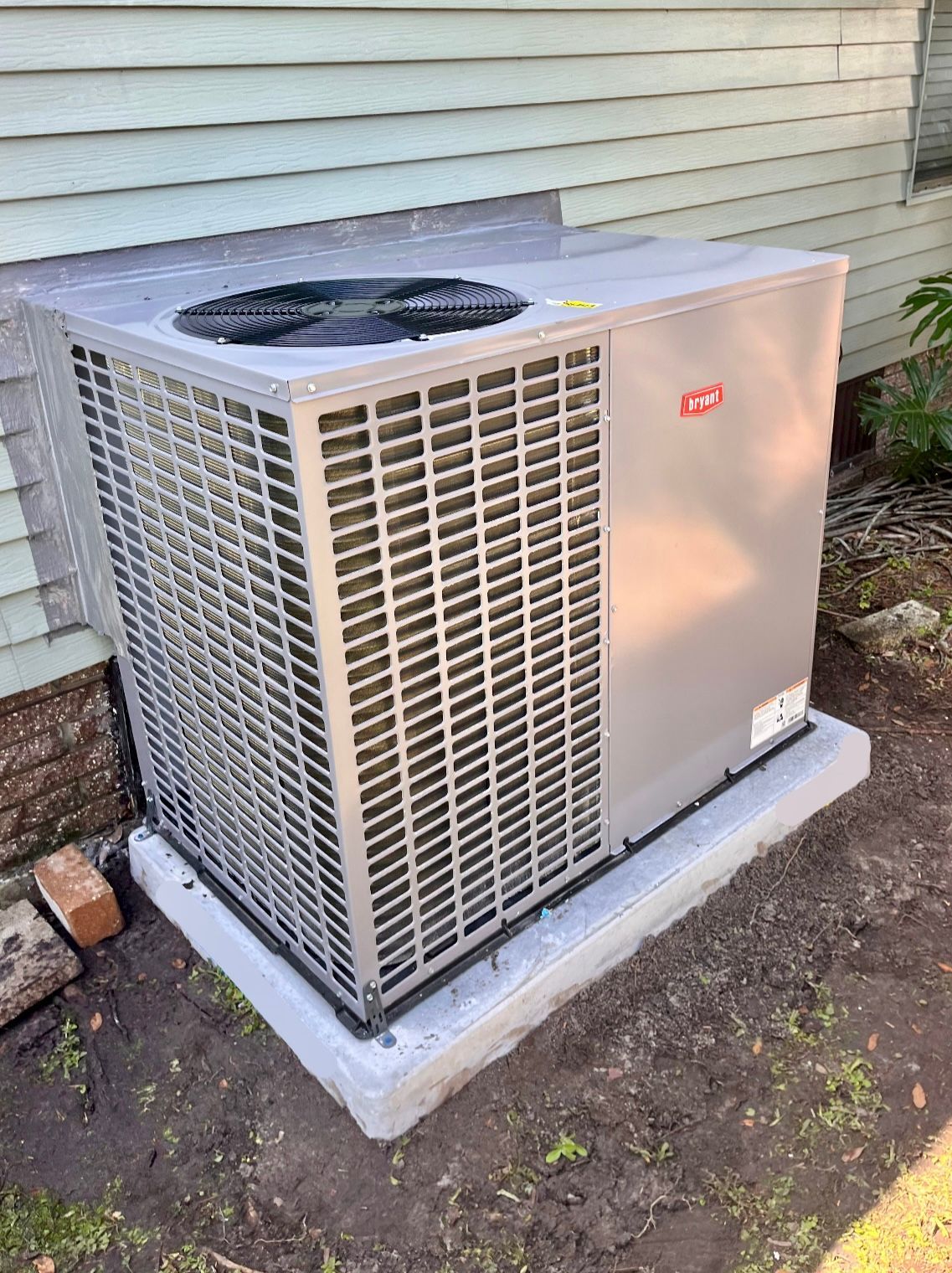 Gray air conditioning unit on a concrete pad next to a house with a light-colored exterior.