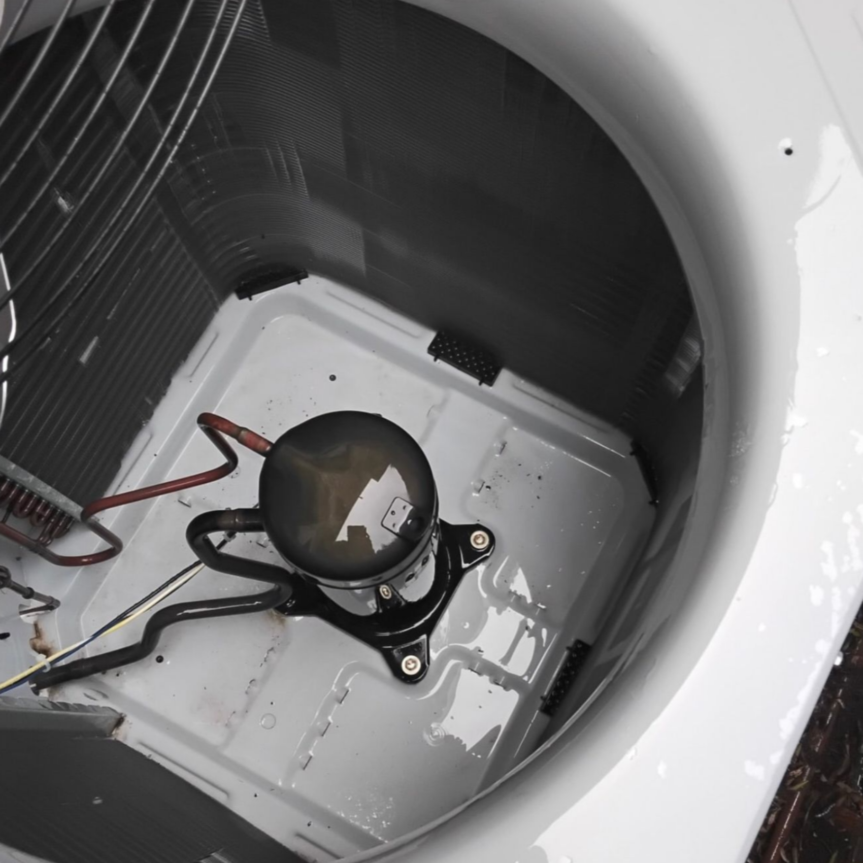 Inside an air conditioning unit, a black compressor is surrounded by water in a white enclosure. Wire and other components are visible.