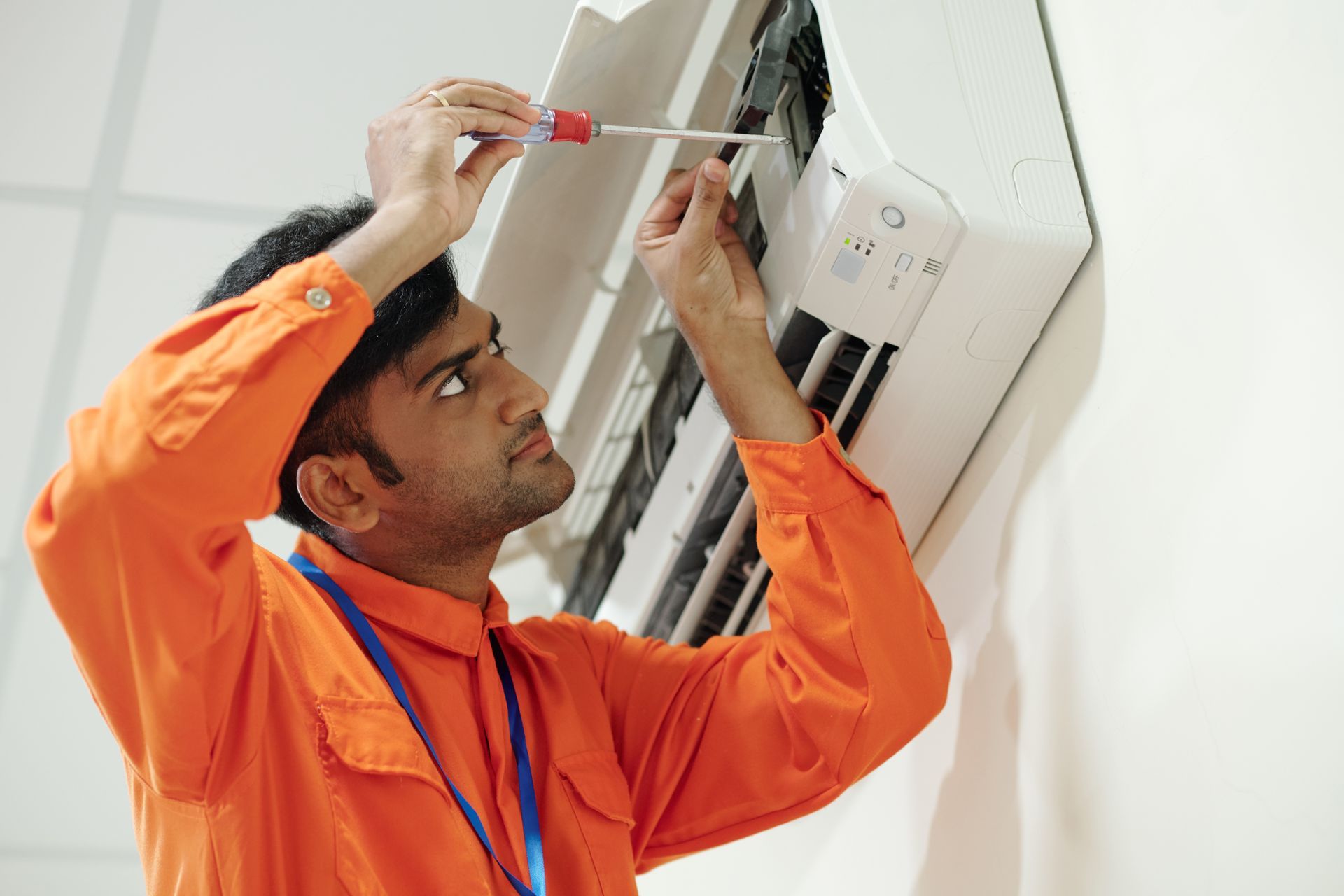 A man is fixing an air conditioner with a screwdriver.